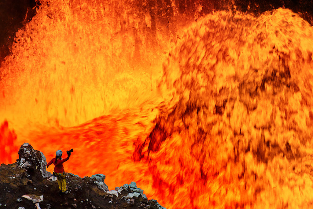 Sprudelnde Lava, unten links ein Steinvorsprung auf dem eine Person mit Kamera in der Hand zu sehen ist