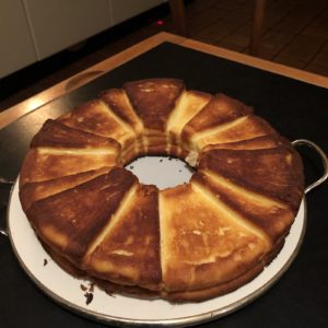 Ein Bild von Ankes Käsekuchen als Ring auf einer weißer Tortenform auf einer schwarzen Platte stehend