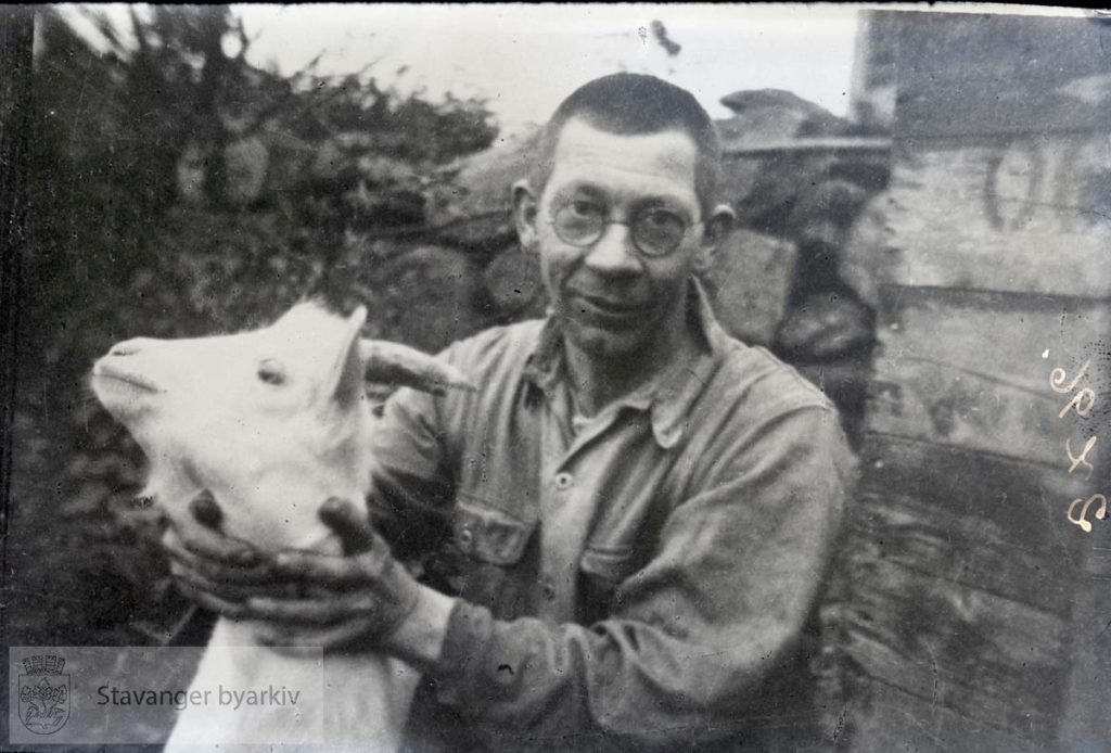 Ein älteres Foto, ein Mann mit Brille halt den Hals eines Ziegenbocks 